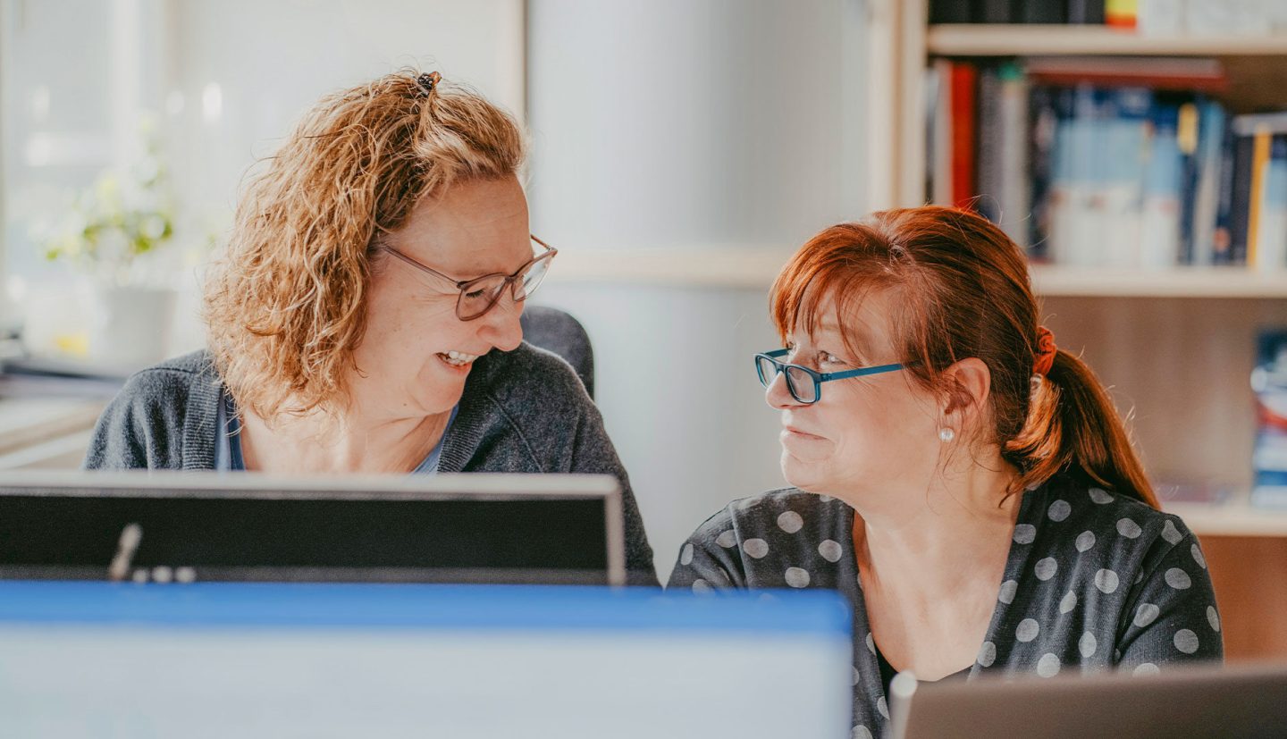 Zwei Mitarbeitende die sich anlachen