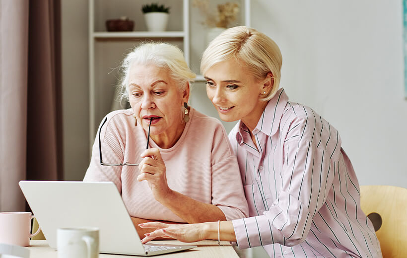 Eine jüngere Frau zeigt einer älteren Frau etwas an einem Laptop